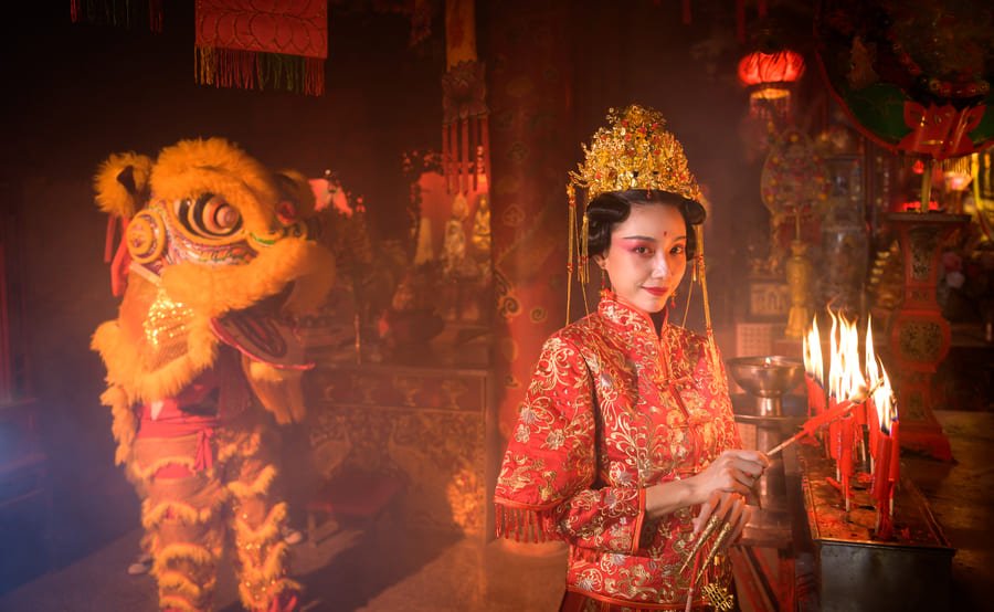 Escena festiva, mística y ricamente detallada de las celebraciones del Año Nuevo Chino en el interior de lo que parece ser un templo tradicional. La atmósfera está impregnada de tonos cálidos y rojizos, envuelta en una suave neblina o humo de incienso que realza la iluminación dramática.