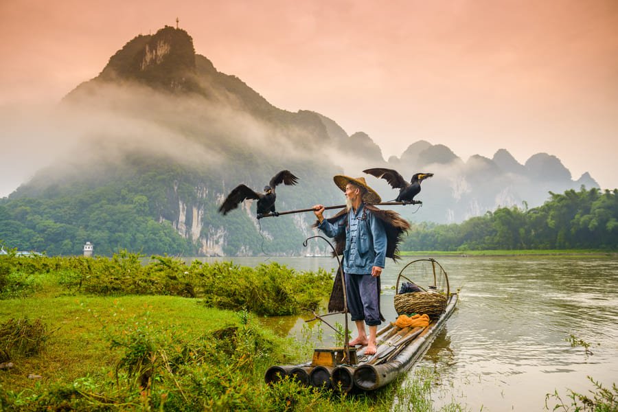 Pescador de cormorán sobre una lancha en el río Yulong en Yangshuo con montaas de fondo.