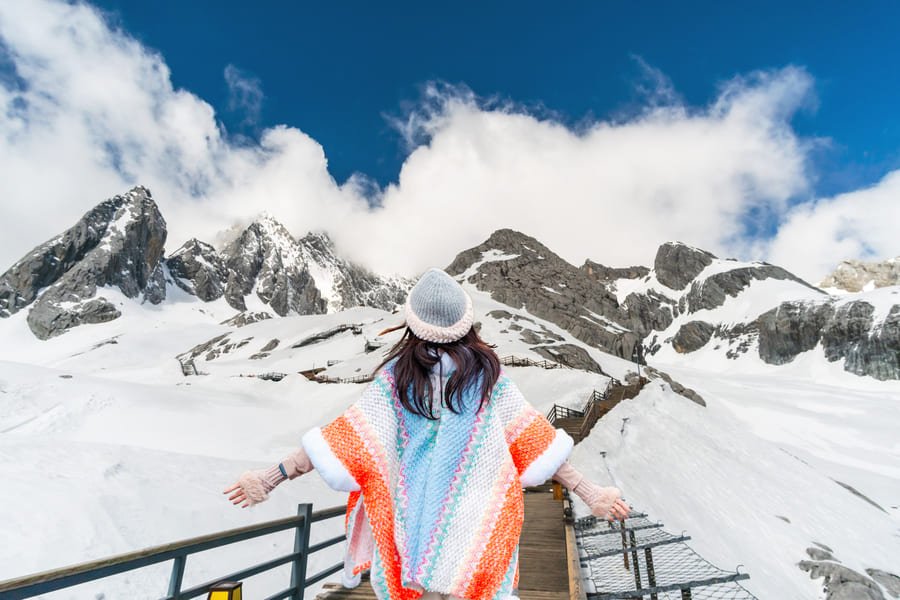 Una mujer con poncho colorido camina por la pasarela de madera de la Montaña Nevada del Dragón de Jade (Yulong Xueshan) en Yunnan, China.